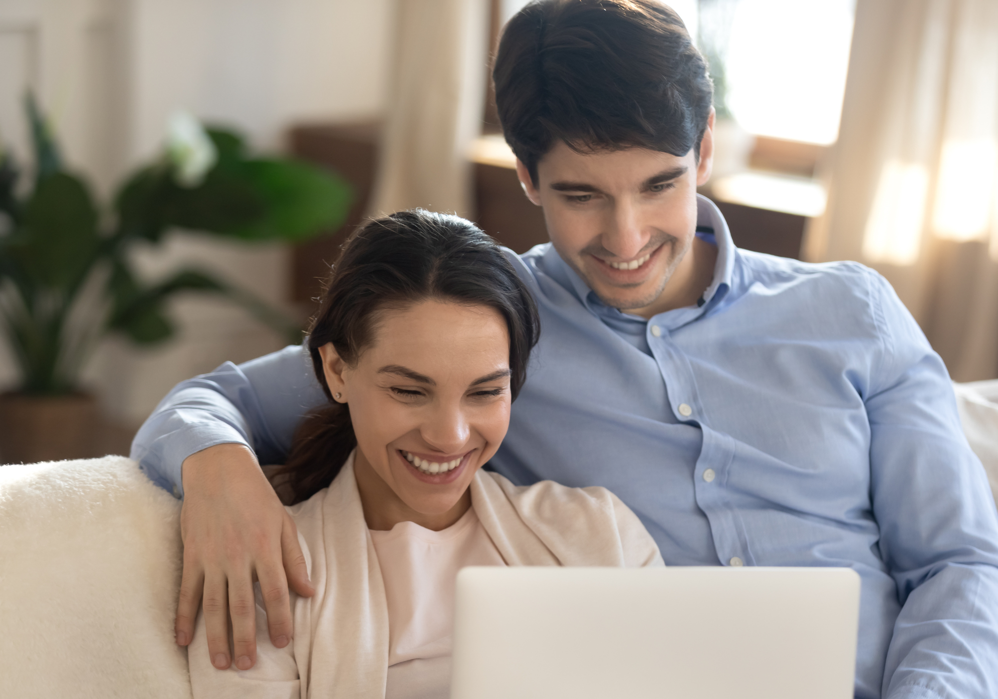 couple sitting on sofa holding credit card and looking at laptop